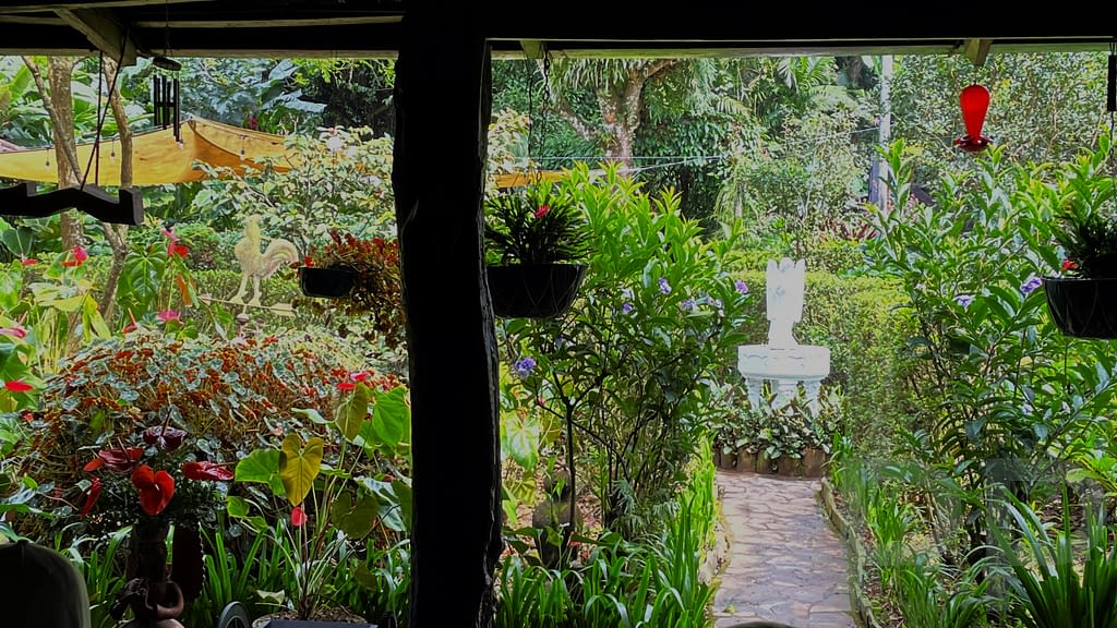 Lush garden with tropical flowers, greenery, and a white statue viewed from the covered patio at El Jardín de Celeste restaurant, Ruta de las Flores, El Salvador.