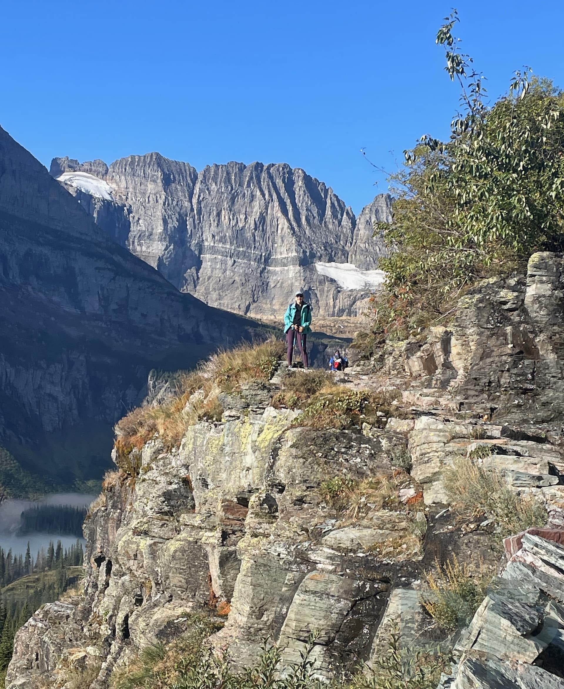 A hiker looks down on the Grinnell Glacier Tail with sheer cliffs as the backdrop in Glacier National Park