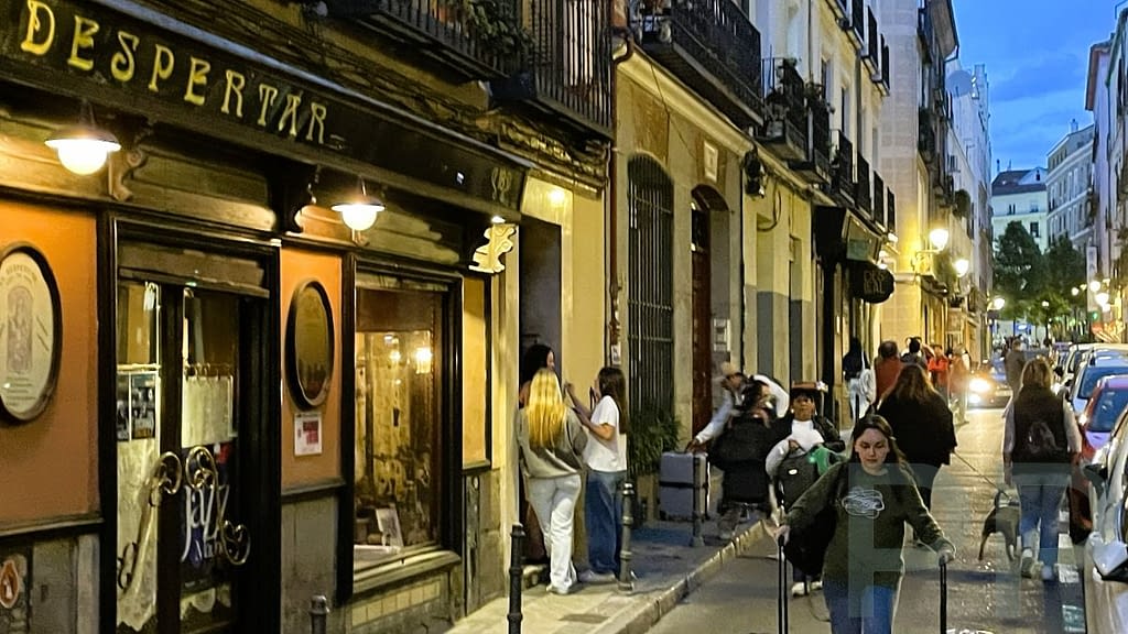 Evening street scene in Madrid with people walking and warm lights from restaurants.