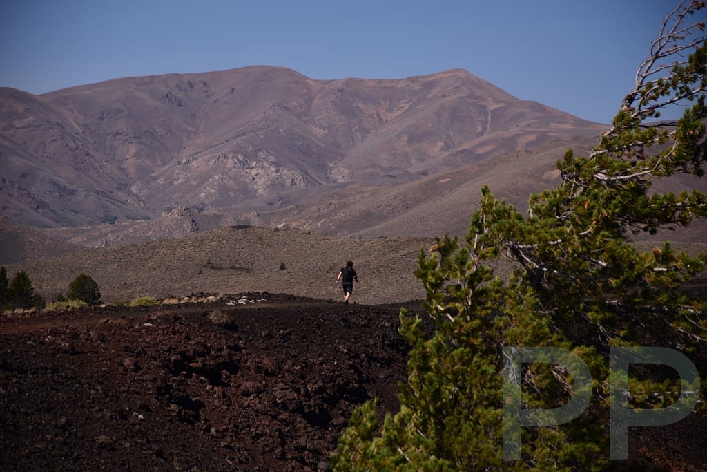 A hiker crossing a wide volcanic landscape with dark lava fields and distant mountains