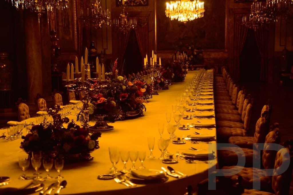 Ornate interior room in the Royal Palace of Madrid with long dining tables and chandeliers.