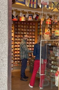 Interior of O Mundo Fant&aacute;stico da Sardinha Portuguesa shop in &Eacute;vora, with colorful tins of sardines stacked on the wall and a staff member explaining options to a visitor.