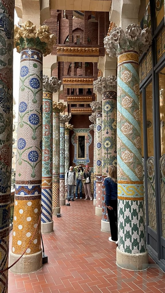 Mosaic-covered columns at the Palau de la Música Catalana in Barcelona, decorated with floral patterns and colorful ceramic tiles in the Modernisme style.