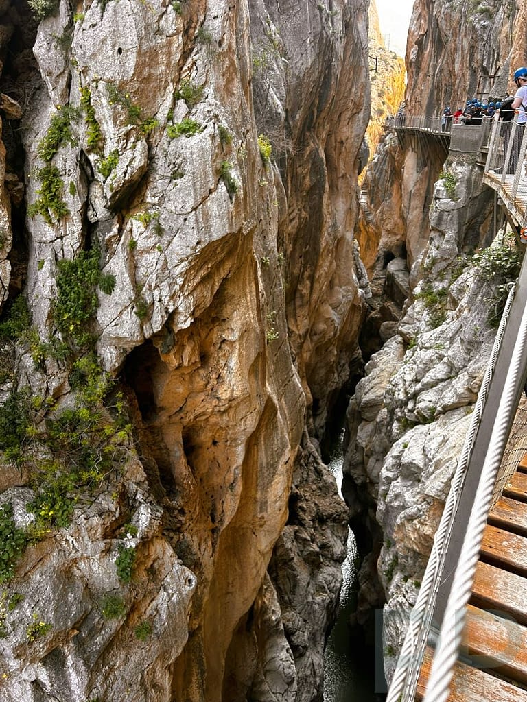 Narrow vertical gorge with the Guadalhorce River far below and hikers on the Caminito del Rey boardwalk above.