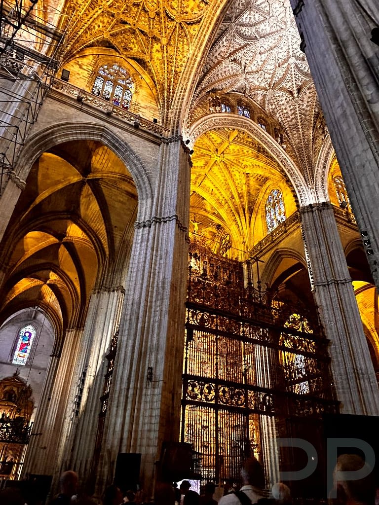 Interior of Seville Cathedral with high ceilings, columns, and dim lighting