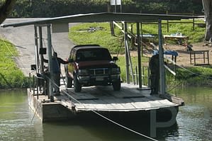 Vehicle crossing a river on a small ferry as part of travel logistics