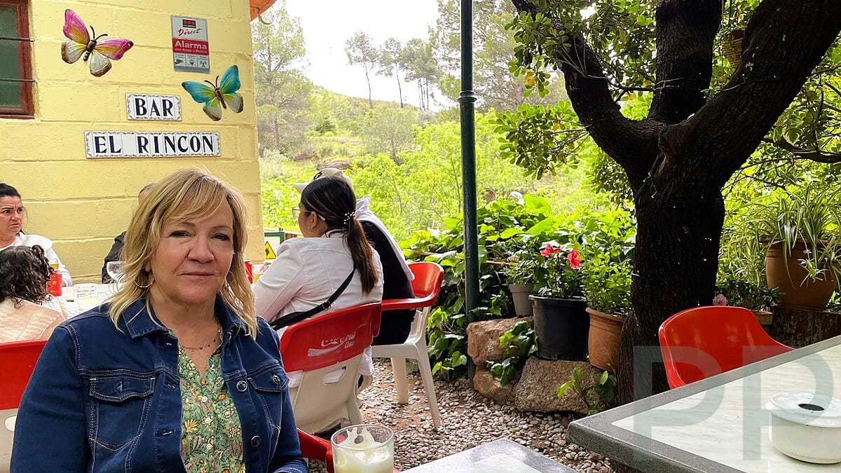 Woman sitting outside Bar El Rincón near Montserrat with the restaurant sign visible behind her