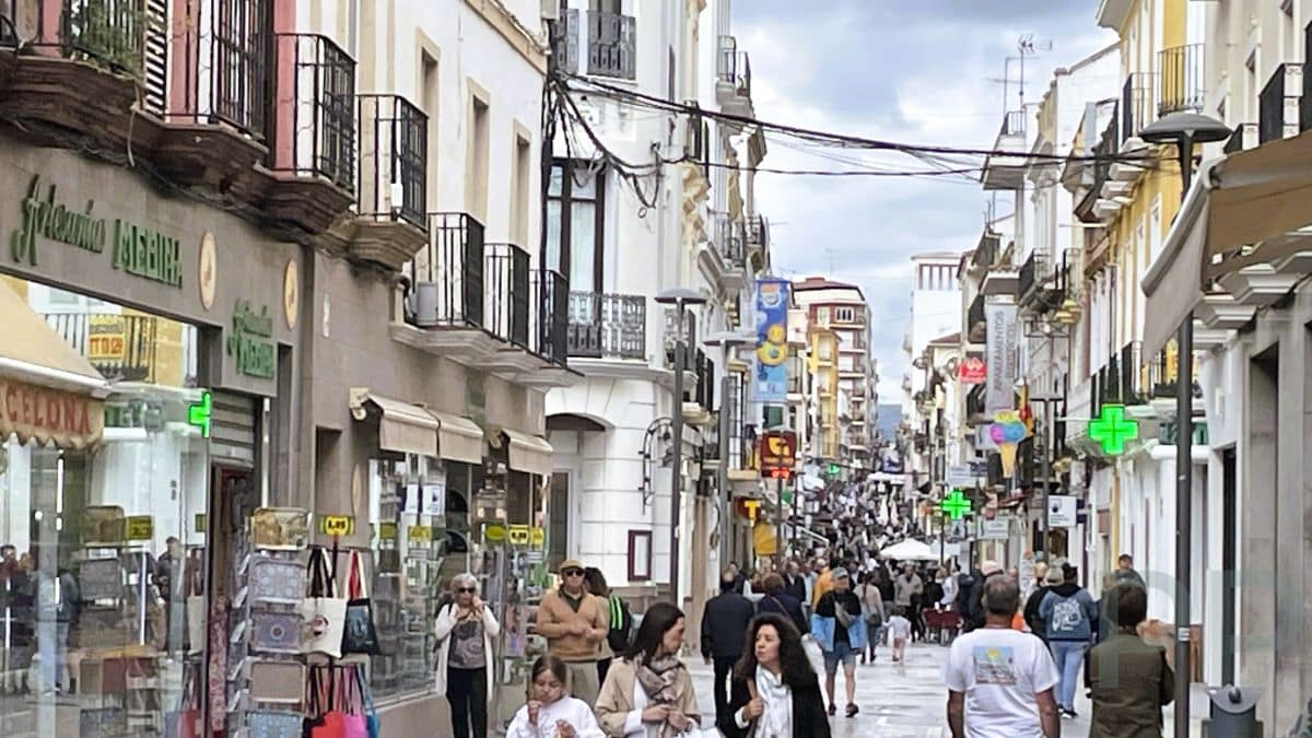 Crowds of people walking along Calle Espinel in Ronda, Spain, a busy pedestrian street with shops and historic balconies.