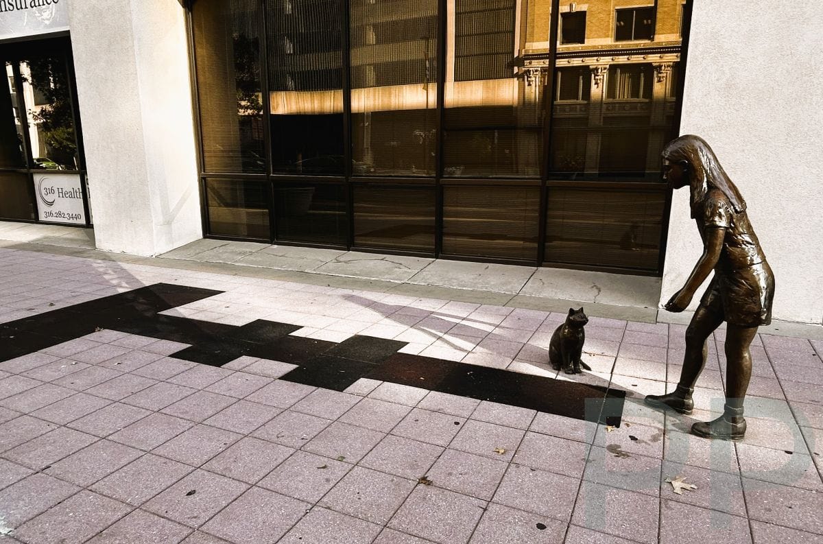 Bronze sculpture of a girl playing hopscotch with a small cat in downtown Wichita.