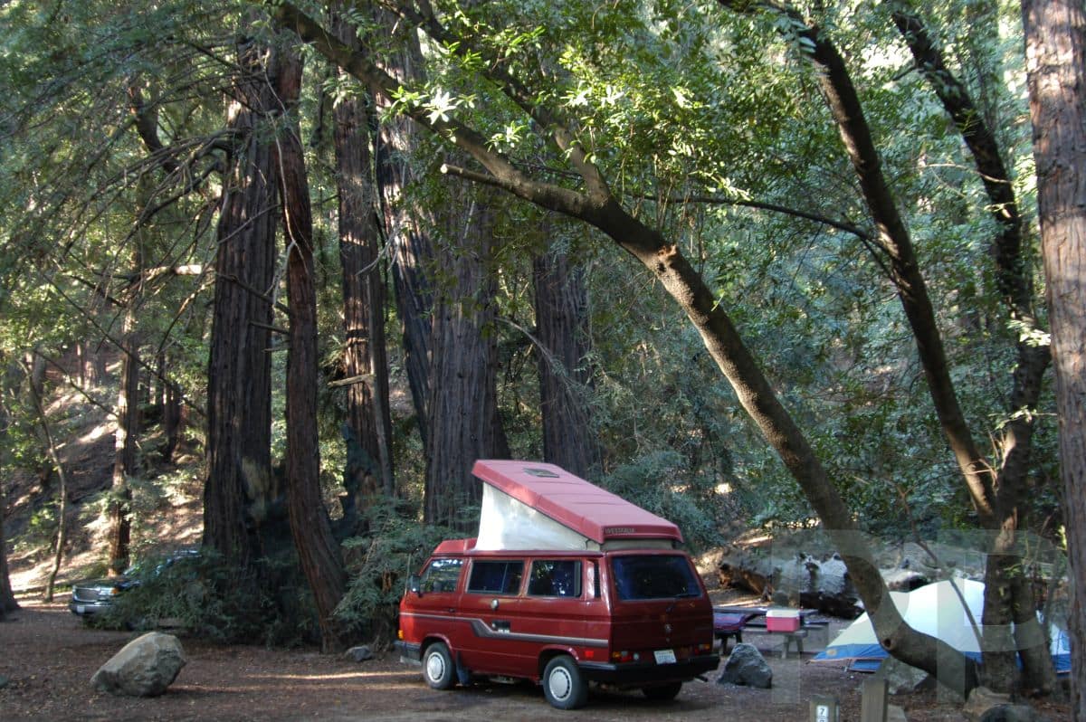 Red campervan with a pop-top roof parked among redwoods in Big Sur.