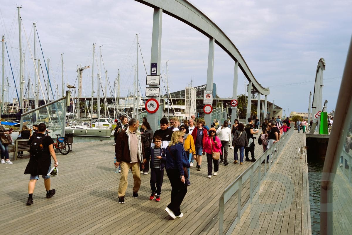 People walking along the Port Vell waterfront in Barcelona beside the marina during the daytime.
