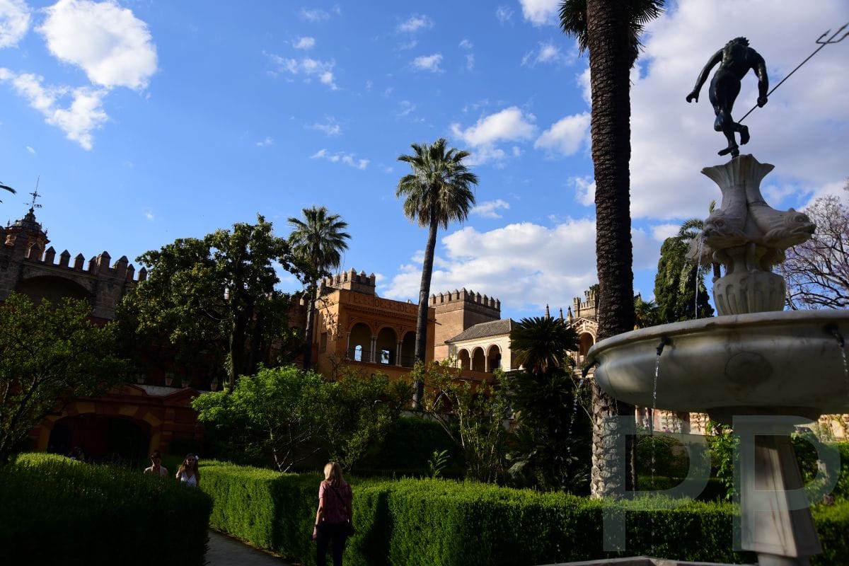 Gardens of the Royal Alc&aacute;zar in Seville with palm trees, hedges, and a decorative fountain