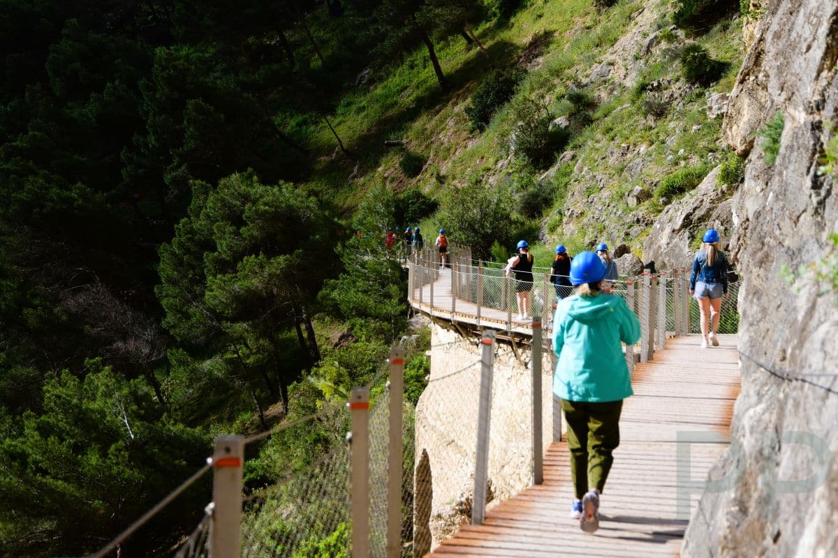 Hikers wearing helmets walking along the wooden walkway of Caminito del Rey in southern Spain