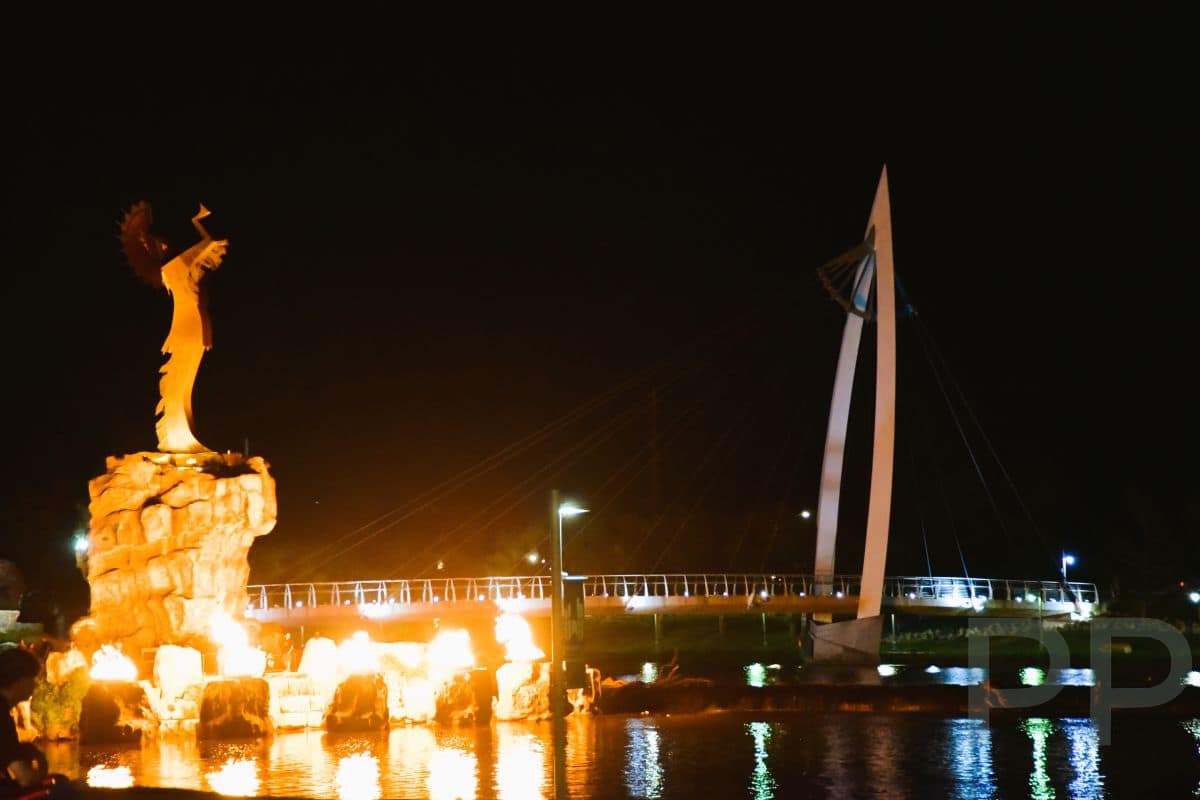 The Keeper of the Plains statue at night with glowing fire rings reflecting on the water in Wichita, Kansas.