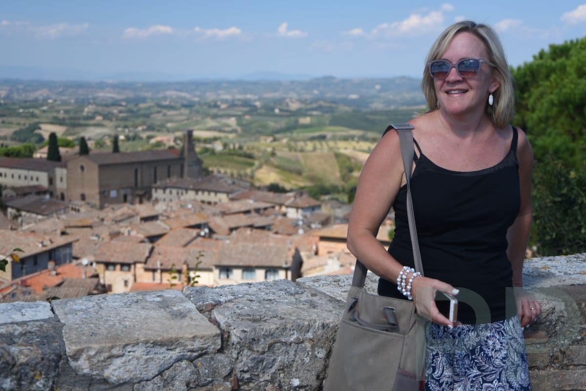 Traveler standing by a stone wall overlooking rooftops and rolling hills in Tuscany, Italy
