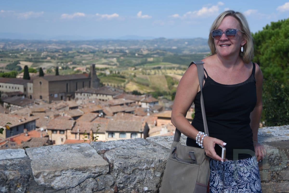 Traveler standing by a stone wall overlooking rooftops and rolling hills in Tuscany, Italy