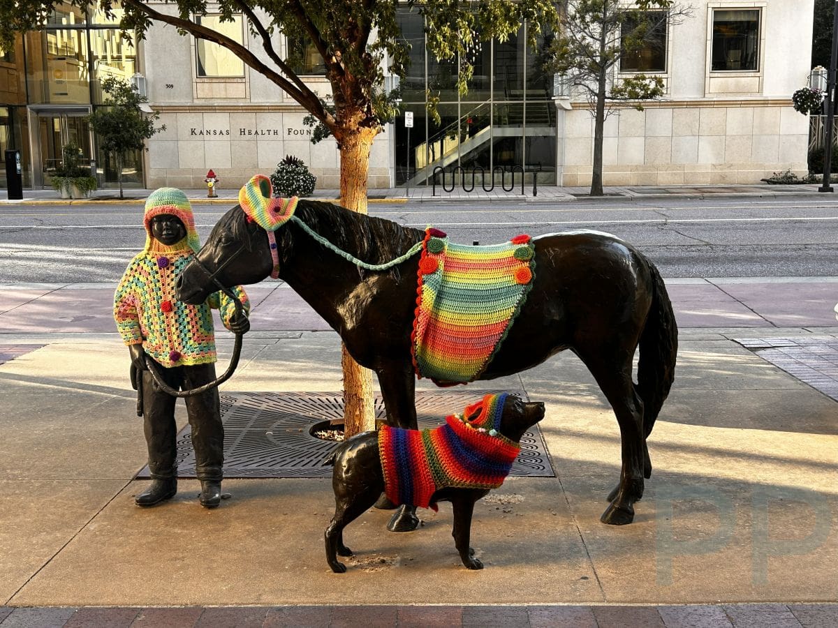 Bronze sculptures of a child, horse, and dog dressed in colorful crocheted coverings in downtown Wichita.