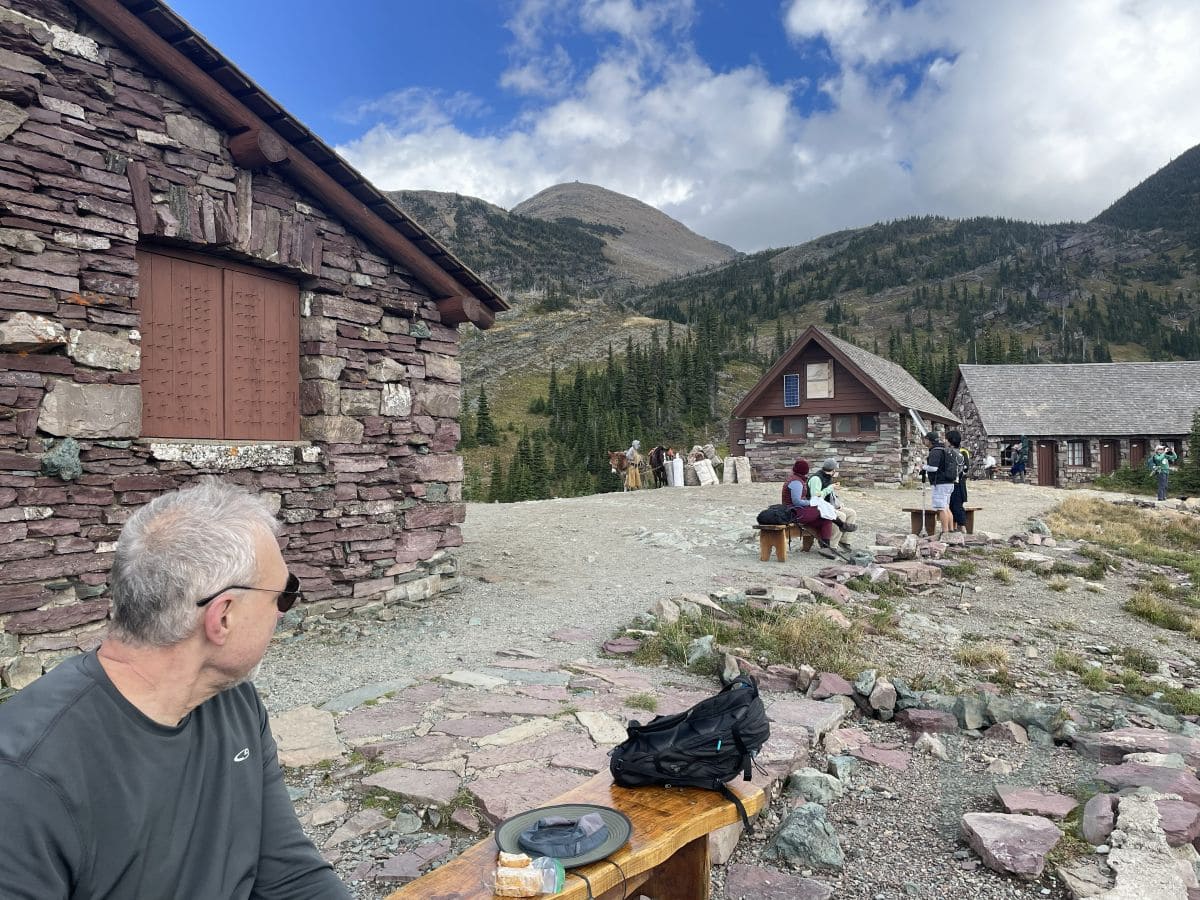 Hikers resting on benches and walkways outside Granite Park Chalet surrounded by alpine scenery.