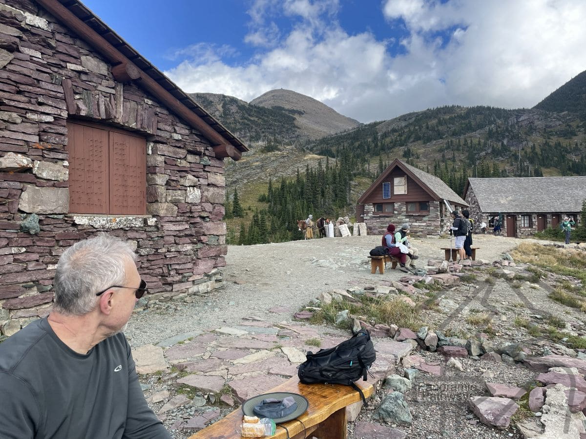 Hikers resting on benches and walkways outside Granite Park Chalet surrounded by alpine scenery.