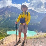 Hiker with trekking poles standing on a rocky trail overlooking turquoise alpine lake in Glacier National Park