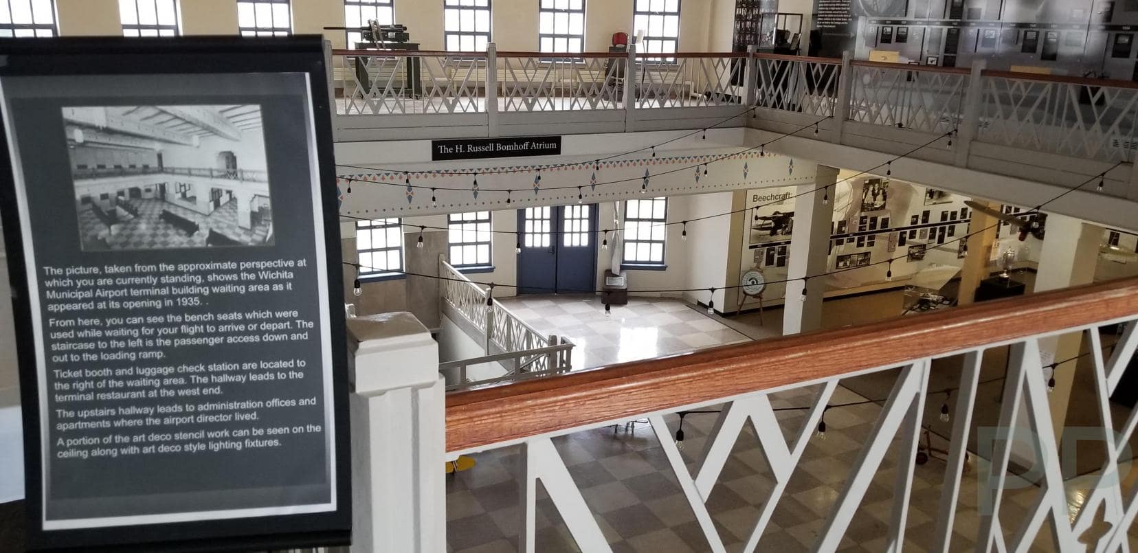 Interior view of the Kansas Aviation Museum&rsquo;s historic 1935 Art Deco airport terminal, showing the two-story atrium with original railings, terrazzo-style floors, tall windows, and interpretive panels describing the building&rsquo;s early years.