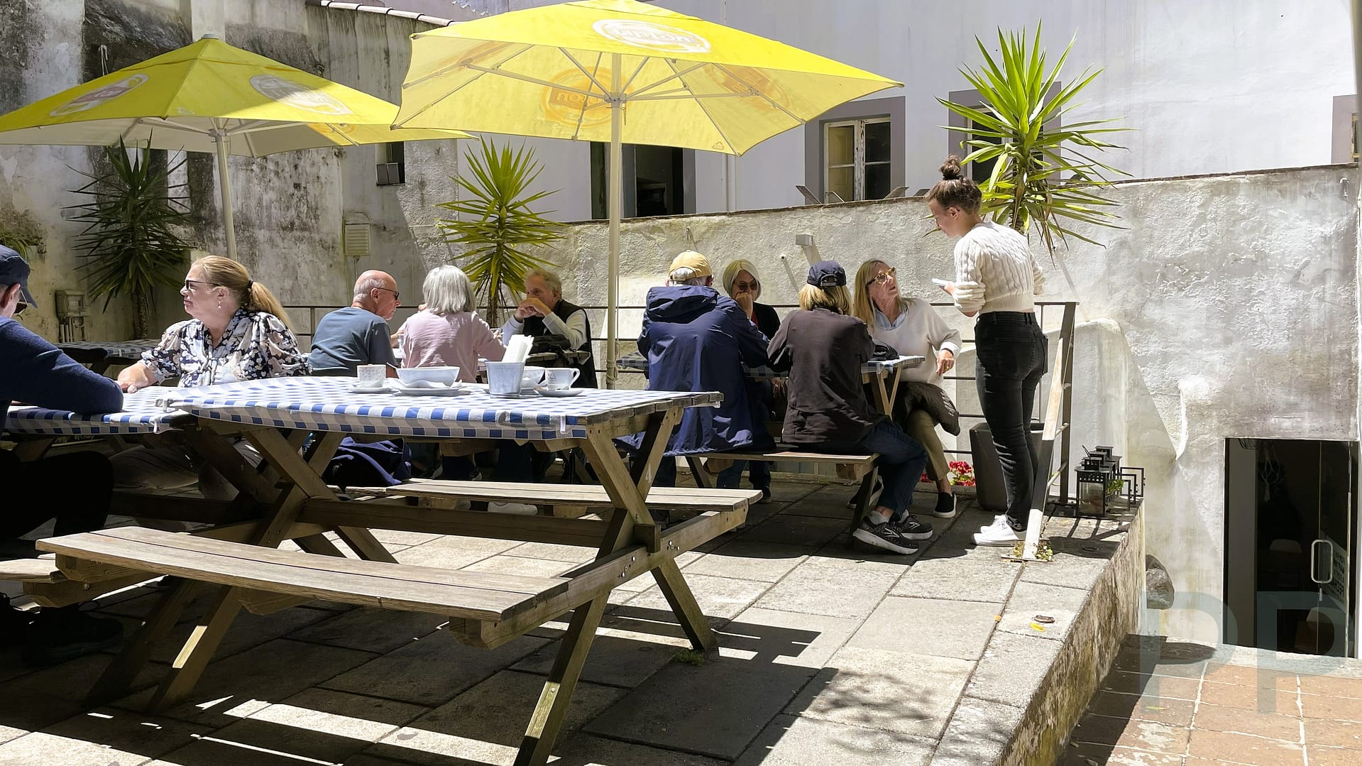 Diners sitting at picnic tables under yellow umbrellas in the secluded patio of The Bakery Lounge in &Eacute;vora, Portugal.
