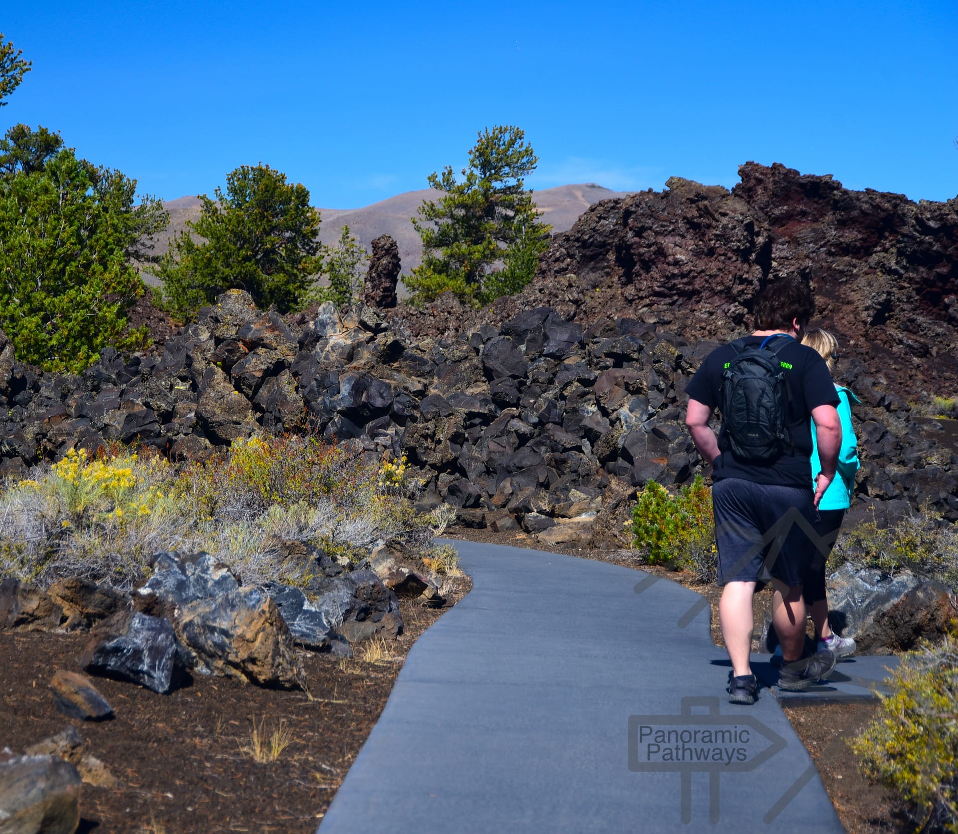 Visitors hiking a paved trail through dark volcanic cinders on the slope of a cinder cone