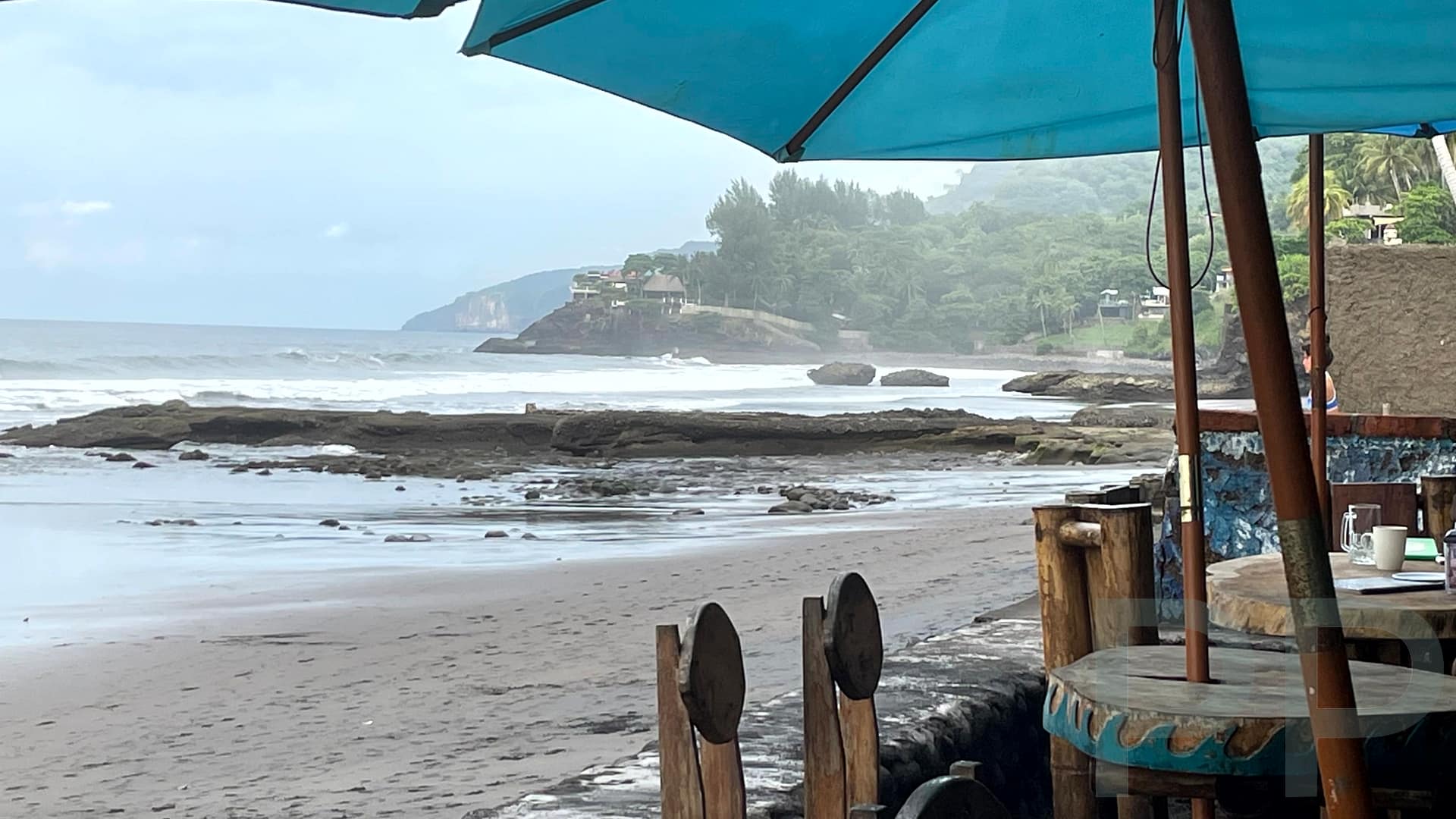 Two-story beachfront café with thatched roof and umbrellas overlooking the ocean in El Zonte, El Salvador.