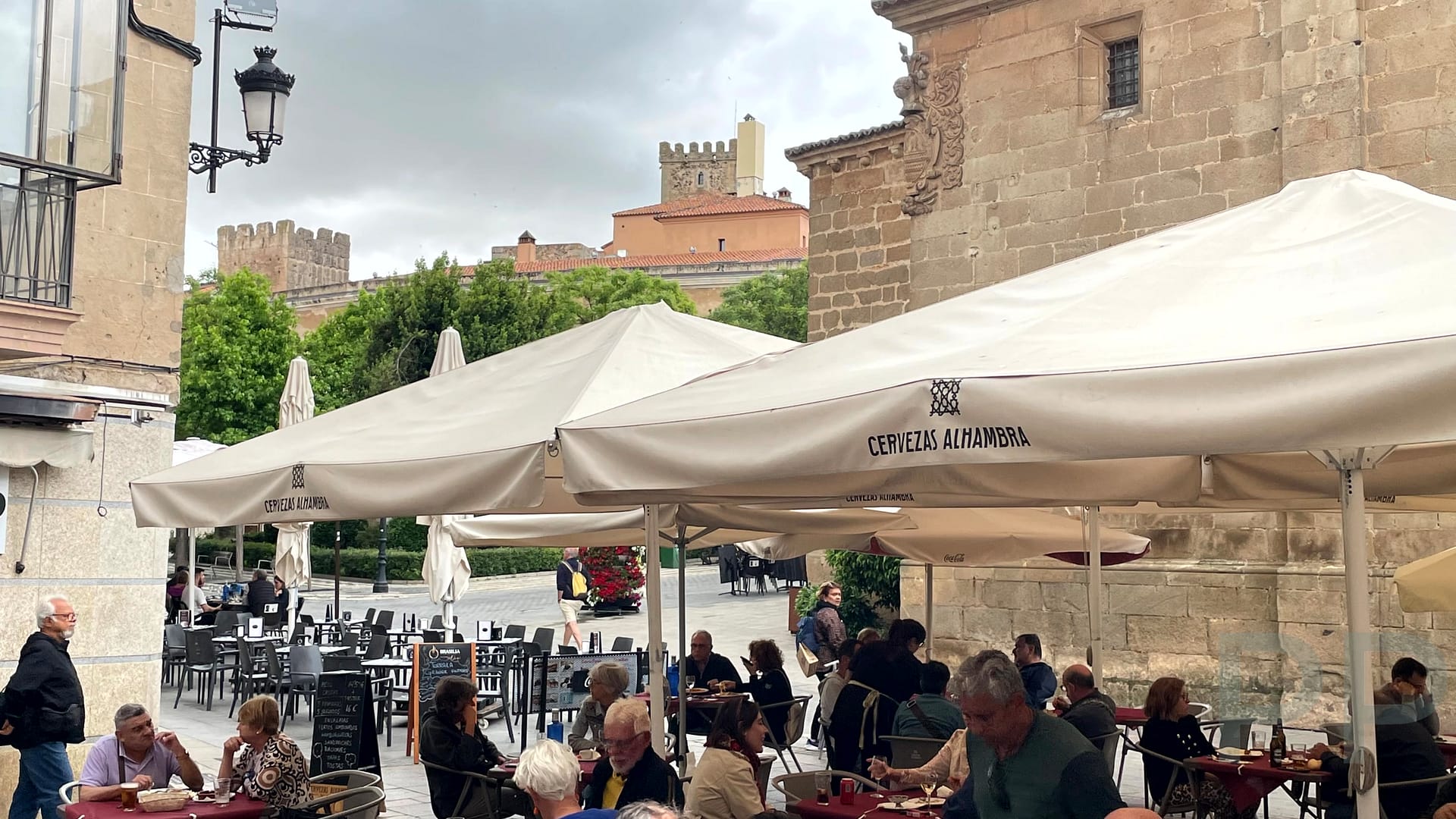 Lively outdoor dining scene in Plaza Mayor, C&aacute;ceres, Spain, with people enjoying tapas at bustling caf&eacute; terraces surrounded by historic buildings.