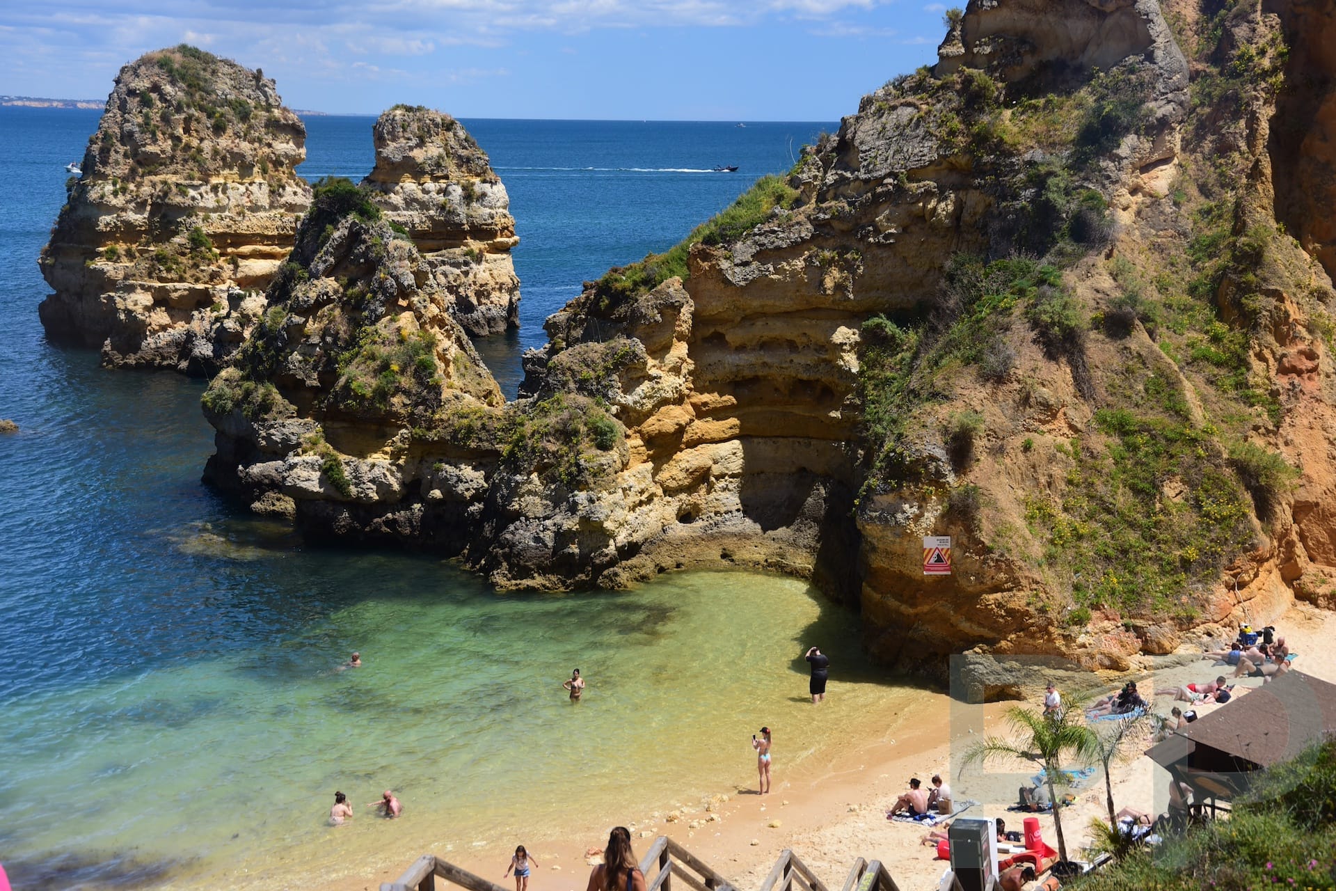 View from cliffs above a beach in Portugal’s Algarve, with dramatic rock formations, turquoise water, and people swimming and sunbathing
