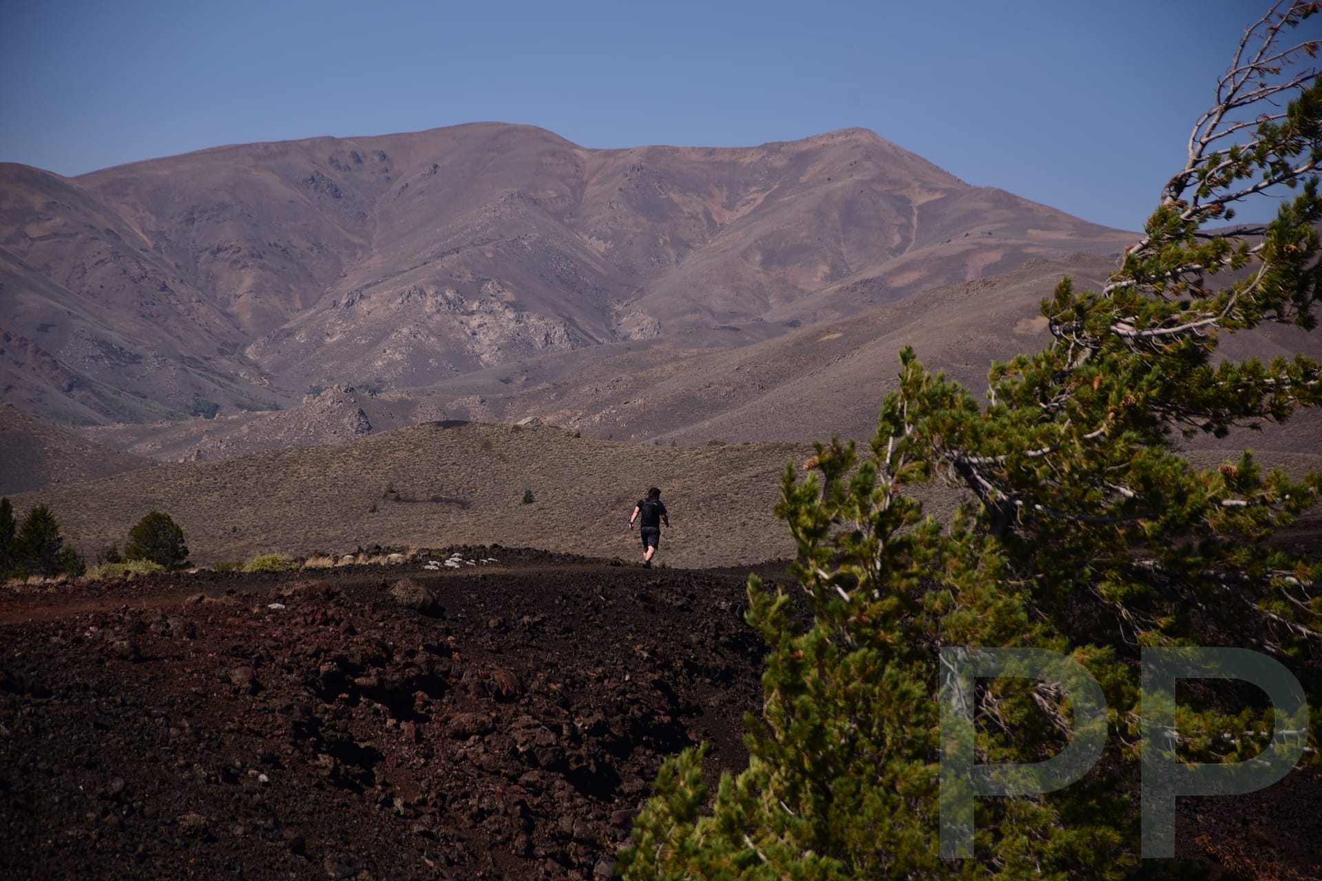 A hiker crossing a wide volcanic landscape with dark lava fields and distant mountains