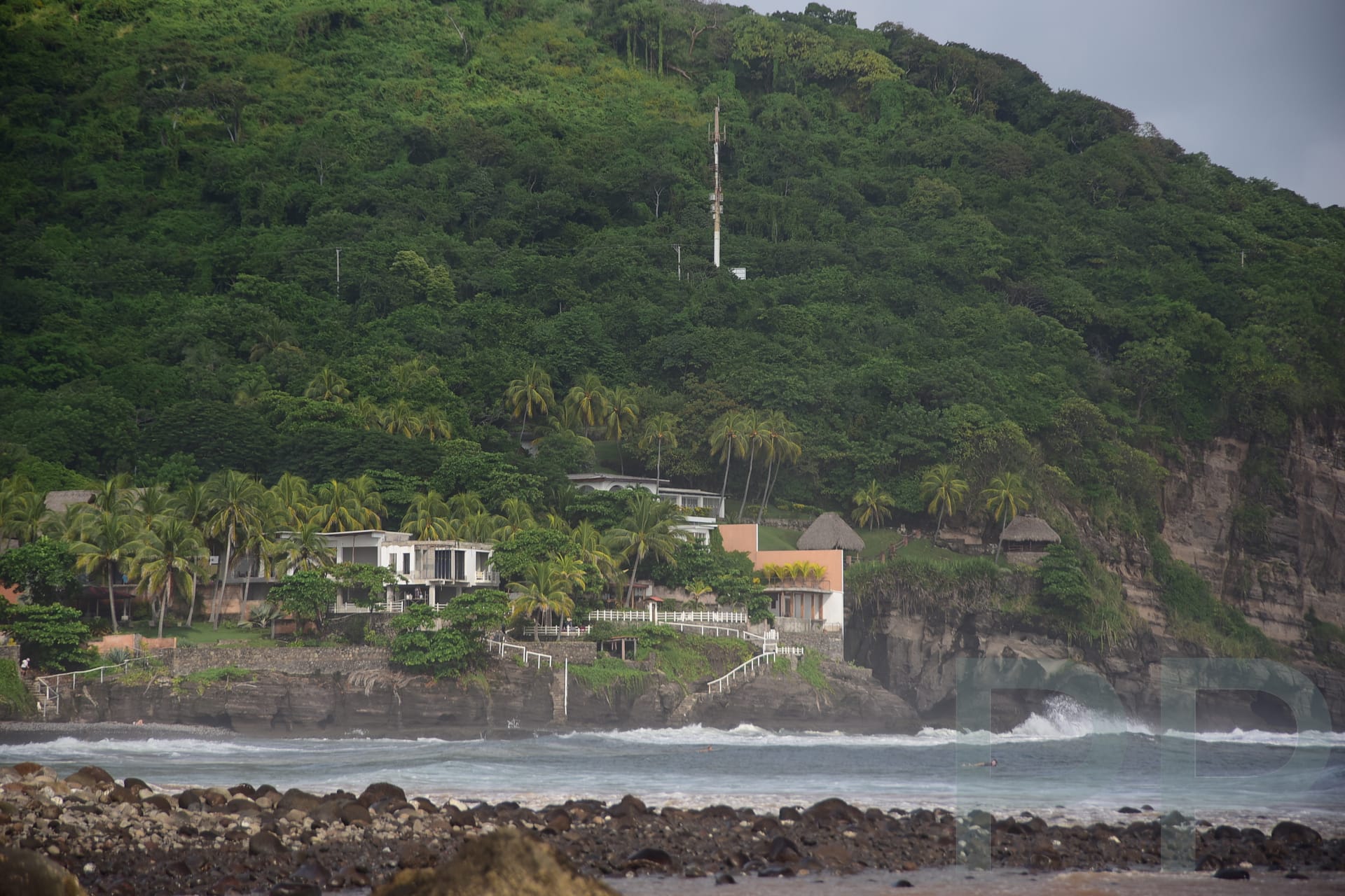 Rocky river mouth and cliffs along El Zonte Beach with a surfer near the shoreline