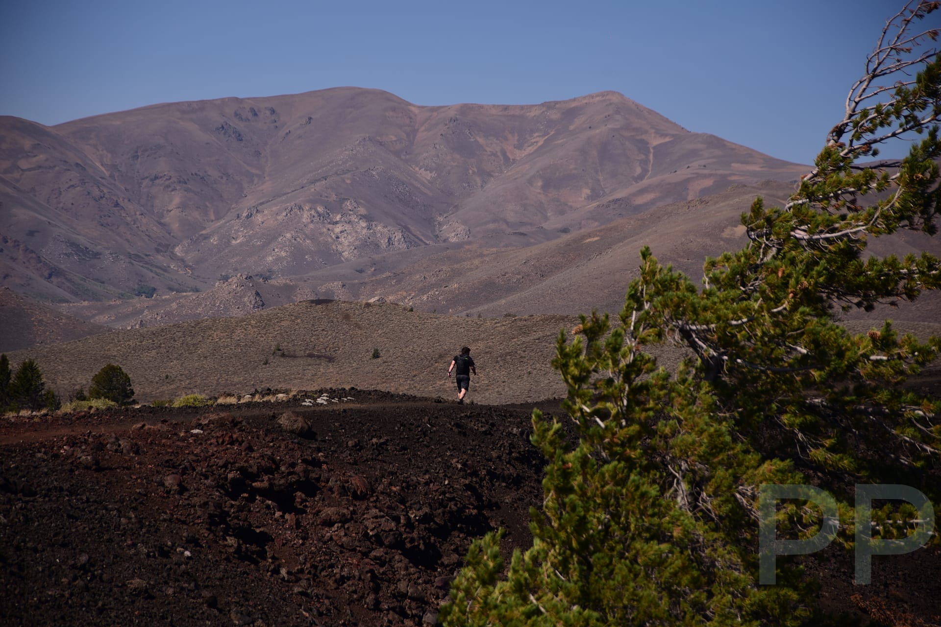 A hiker crossing a wide volcanic landscape with dark lava fields and distant mountains