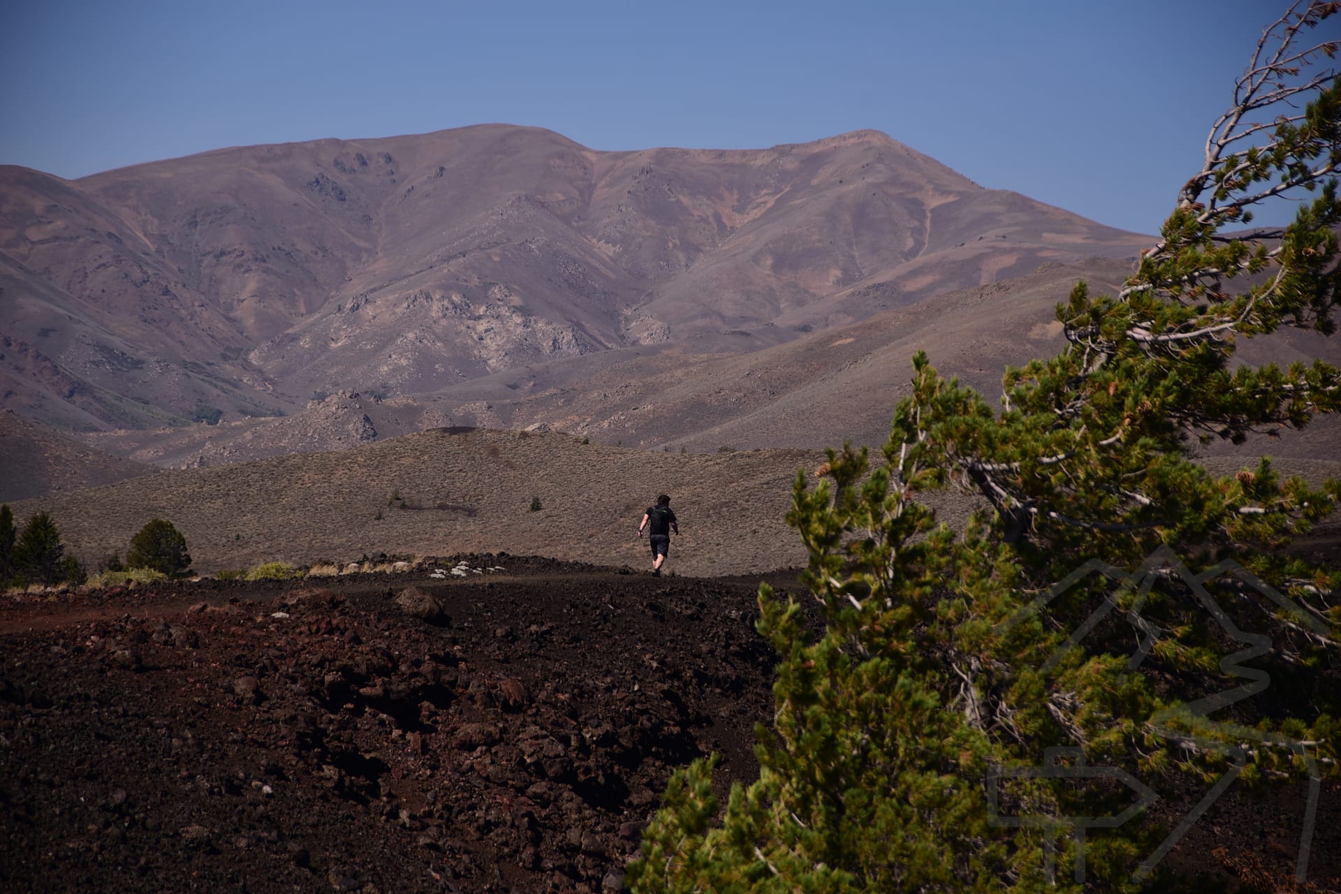 A hiker crossing a wide volcanic landscape with dark lava fields and distant mountains