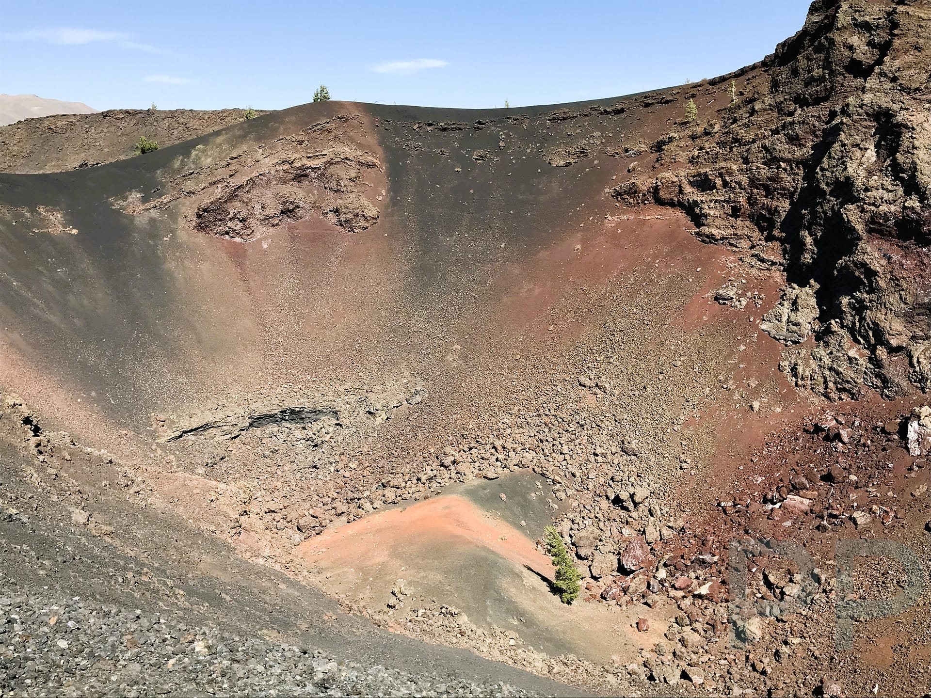 View into a volcanic cinder cone crater showing layered lava and reddish interior rock