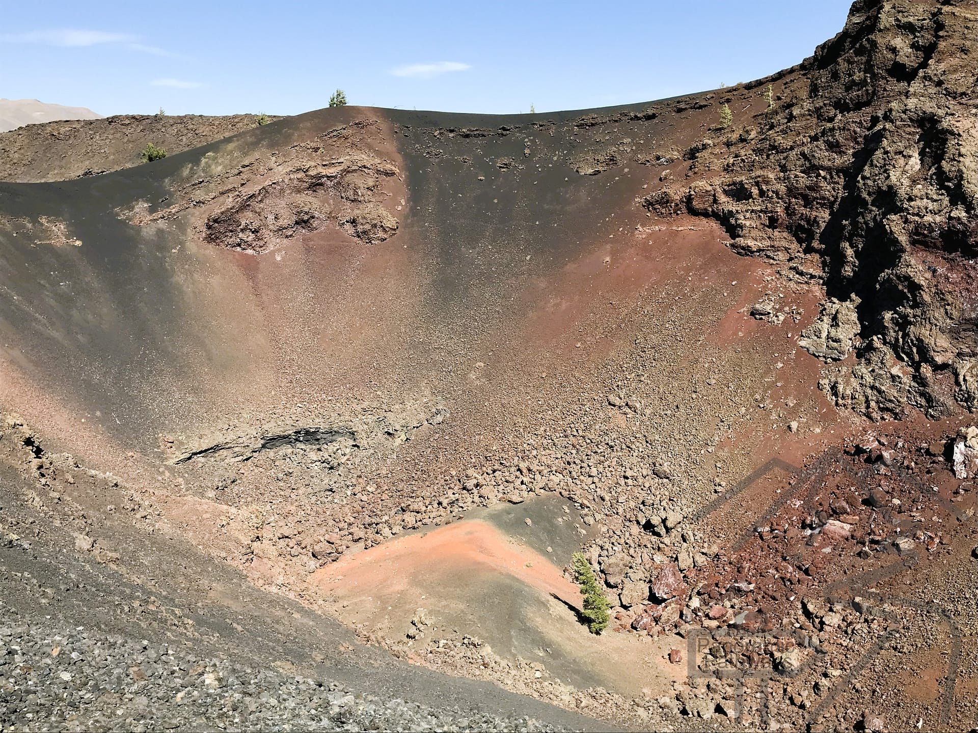 View into a volcanic cinder cone crater showing layered lava and reddish interior rock