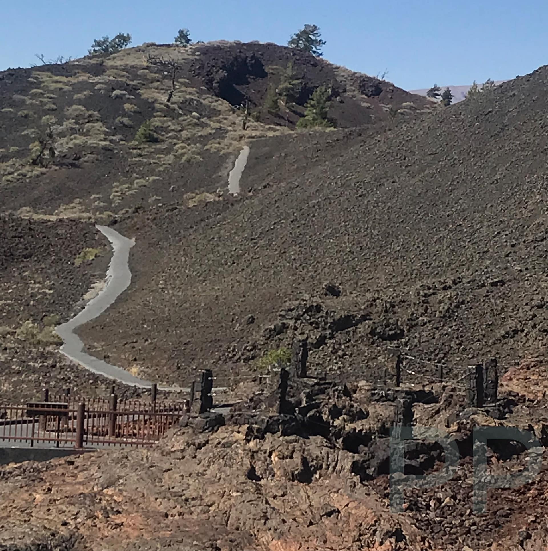 A winding paved trail cutting across a steep volcanic slope formed by cinder and lava