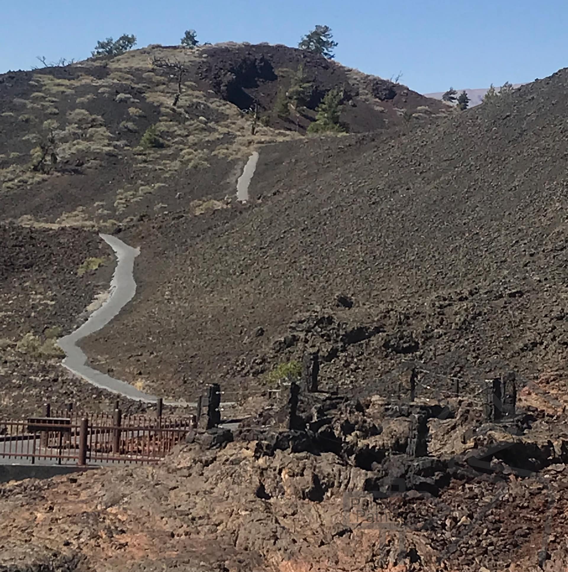 A winding paved trail cutting across a steep volcanic slope formed by cinder and lava