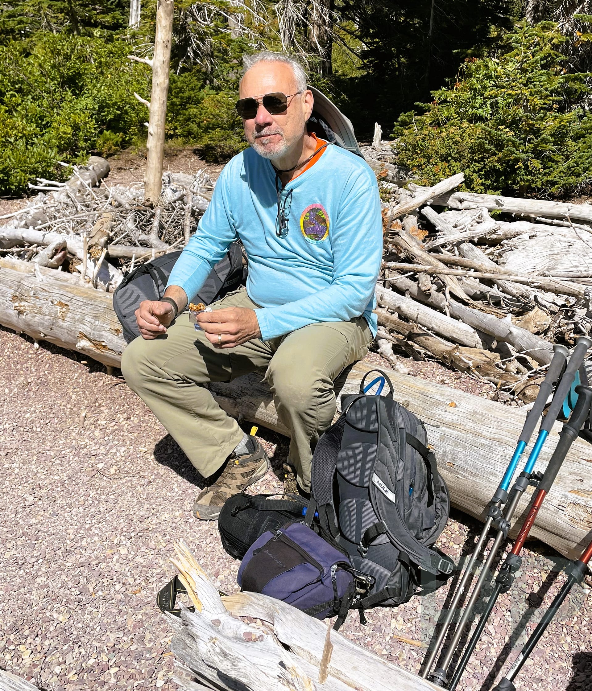 Man resting with hiking poles and backpack during a mountain trail break, symbolizing seasoned travel experience.