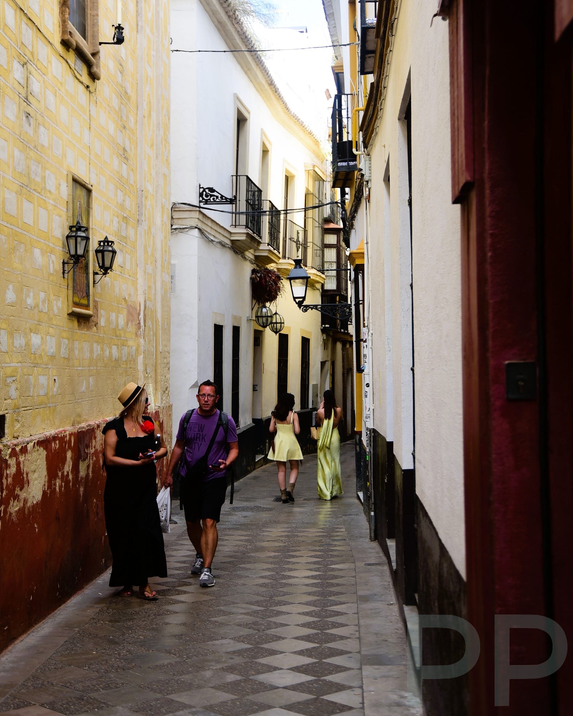 Narrow street in Seville with stone walls, plants, and shaded walkway