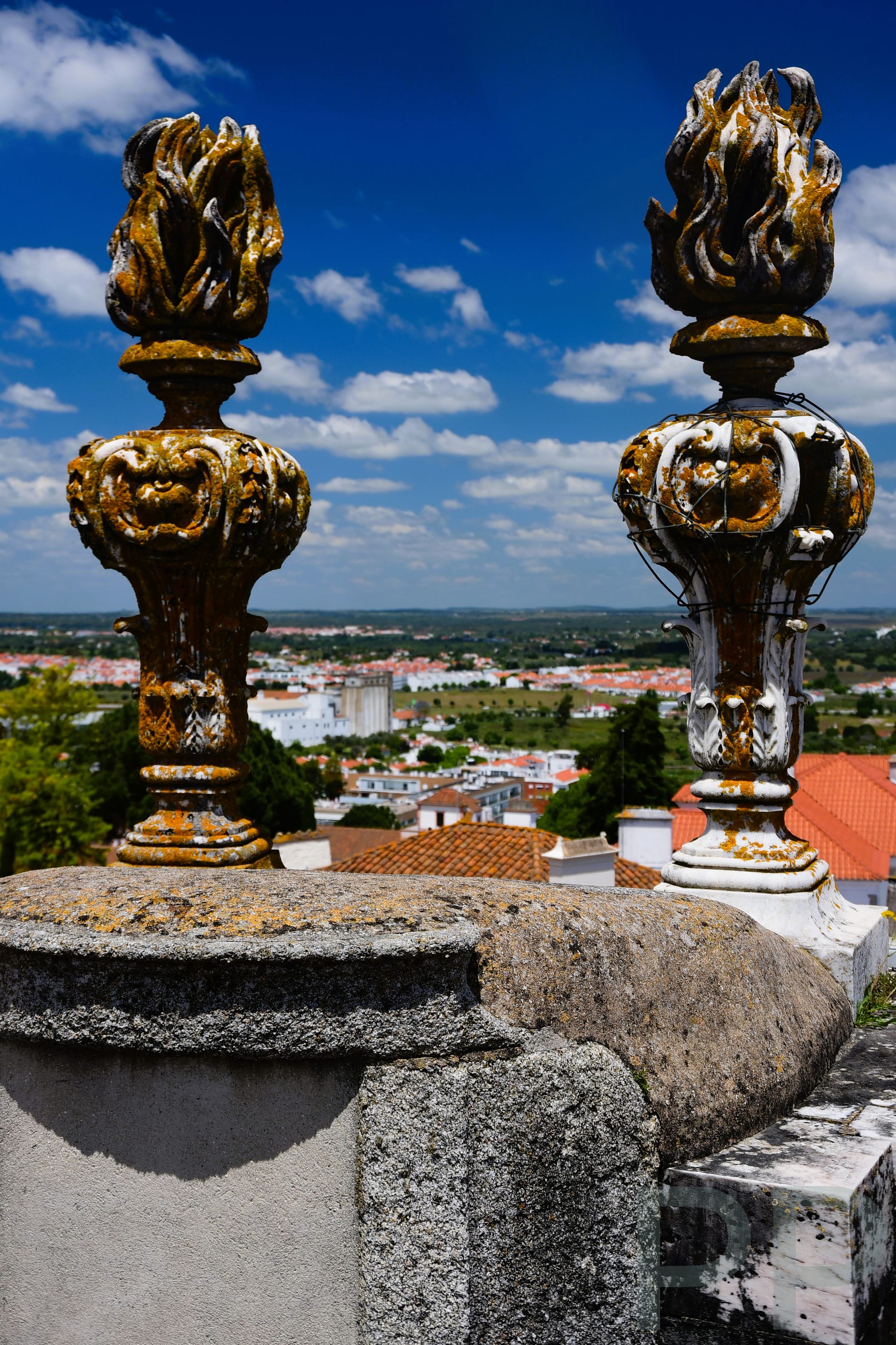Decorative stone finials shaped like flames on the rooftop of Évora Cathedral with views of the city and countryside beyond.
