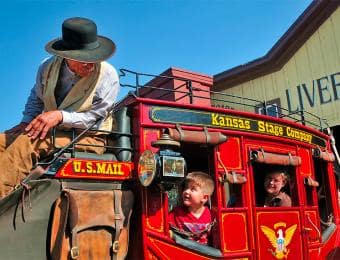 Children riding inside a bright red Kansas Stage Company stagecoach at Old Cowtown Museum while a costumed driver sits atop the coach.