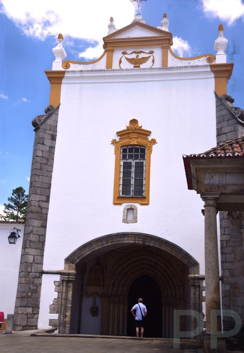 Entrance to Igreja de São Francisco in Évora, Portugal, with a white façade trimmed in yellow and a visitor standing at the arched doorway.