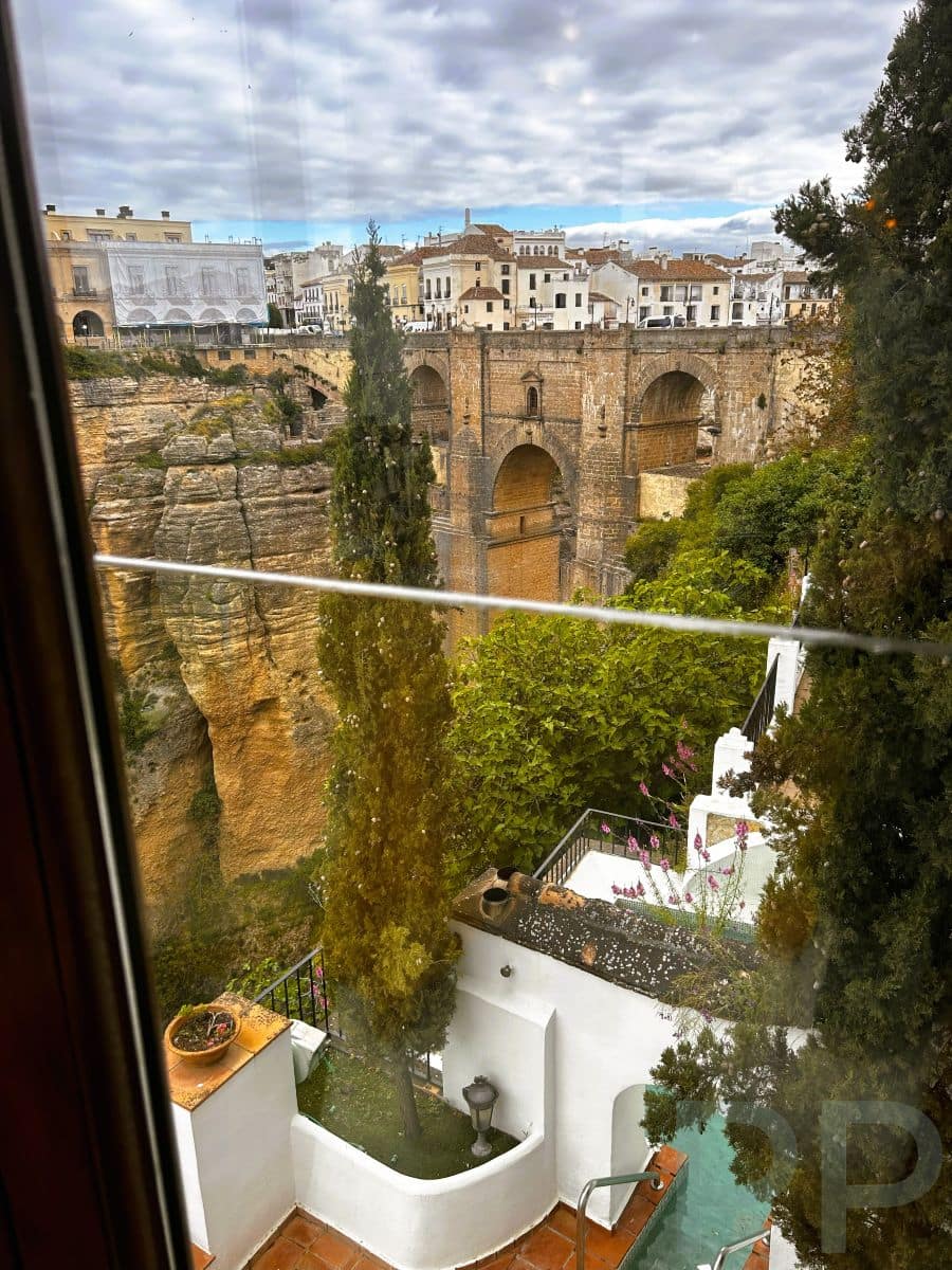 View of Ronda’s Puente Nuevo bridge through the window of Hotel Montelirio, with whitewashed terraces and a pool in the foreground.