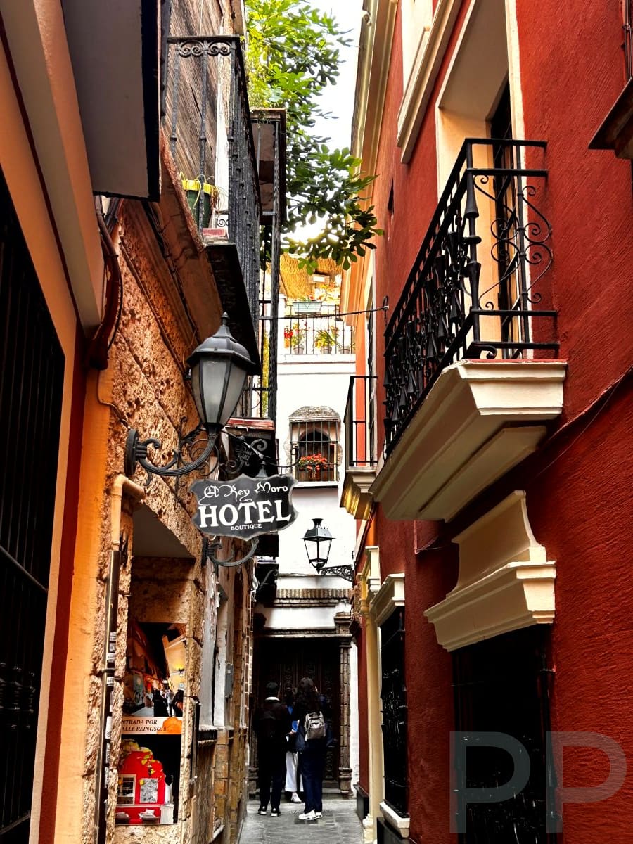 Narrow alley in Barrio Santa Cruz with balconies, lanterns, and colorful buildings