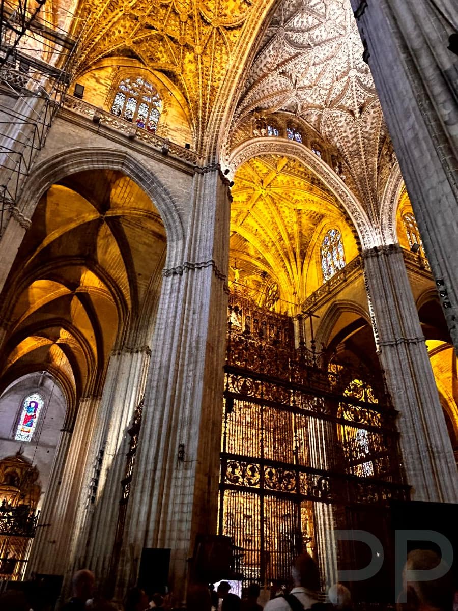 Interior of Seville Cathedral with high ceilings, columns, and dim lighting