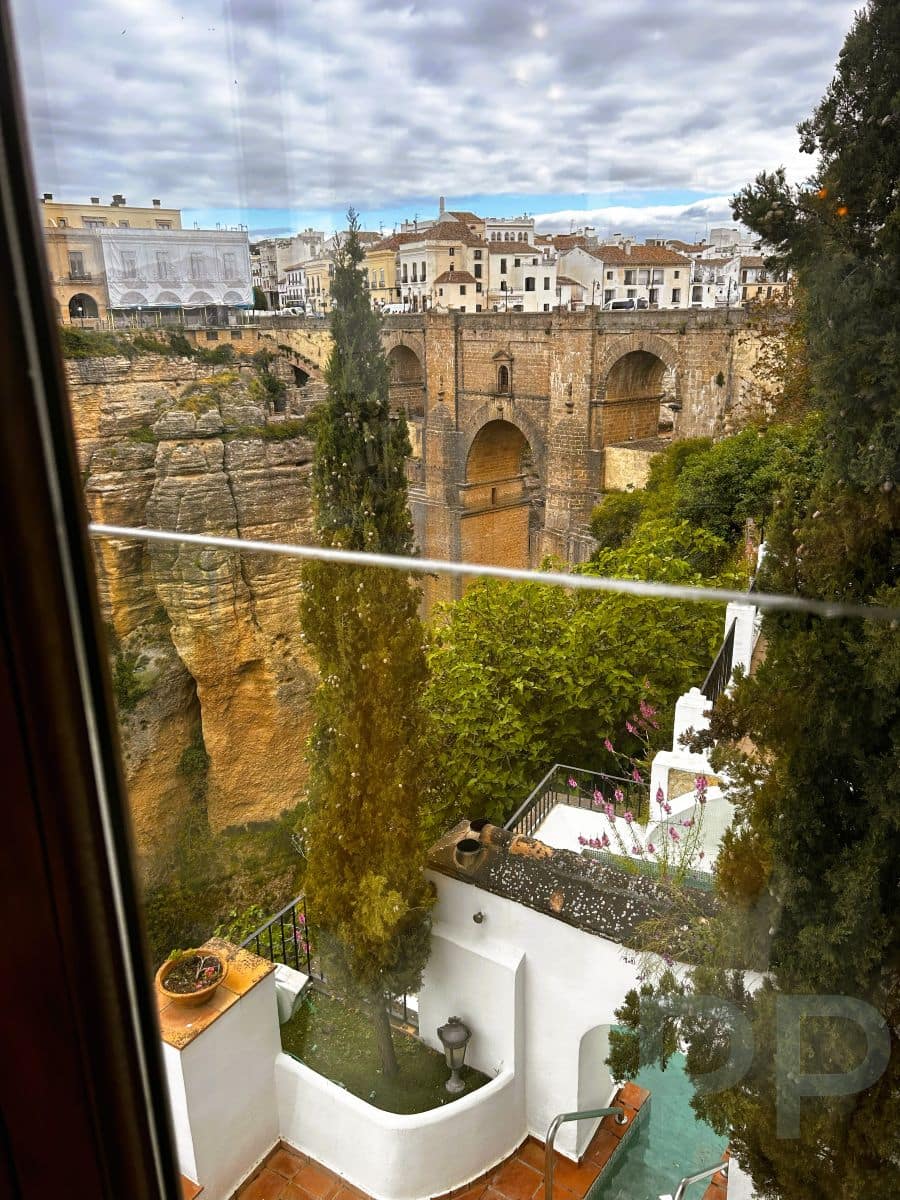 View of Ronda&rsquo;s Puente Nuevo bridge through the window of Hotel Montelirio, with whitewashed terraces and a pool in the foreground.