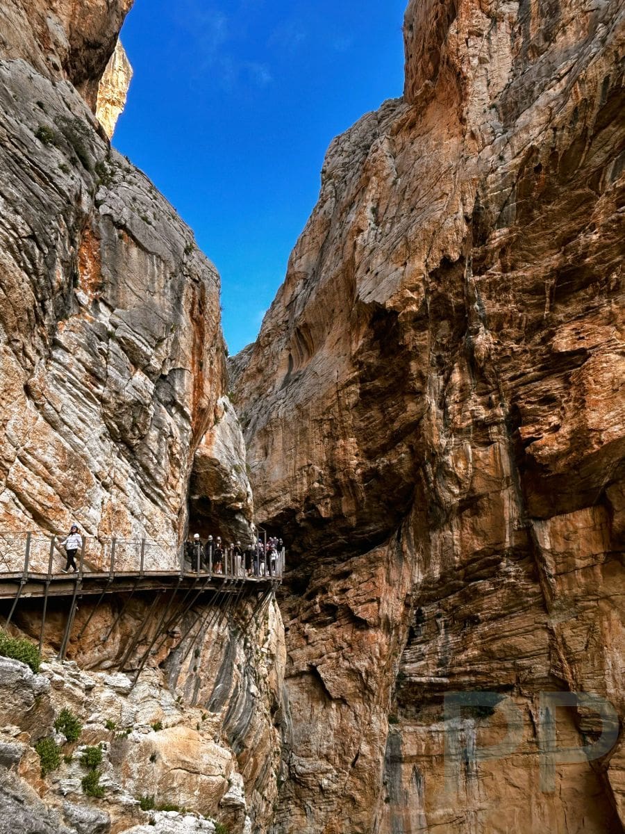 Hikers walking along the Caminito del Rey boardwalk attached to sheer limestone cliffs in Spain.