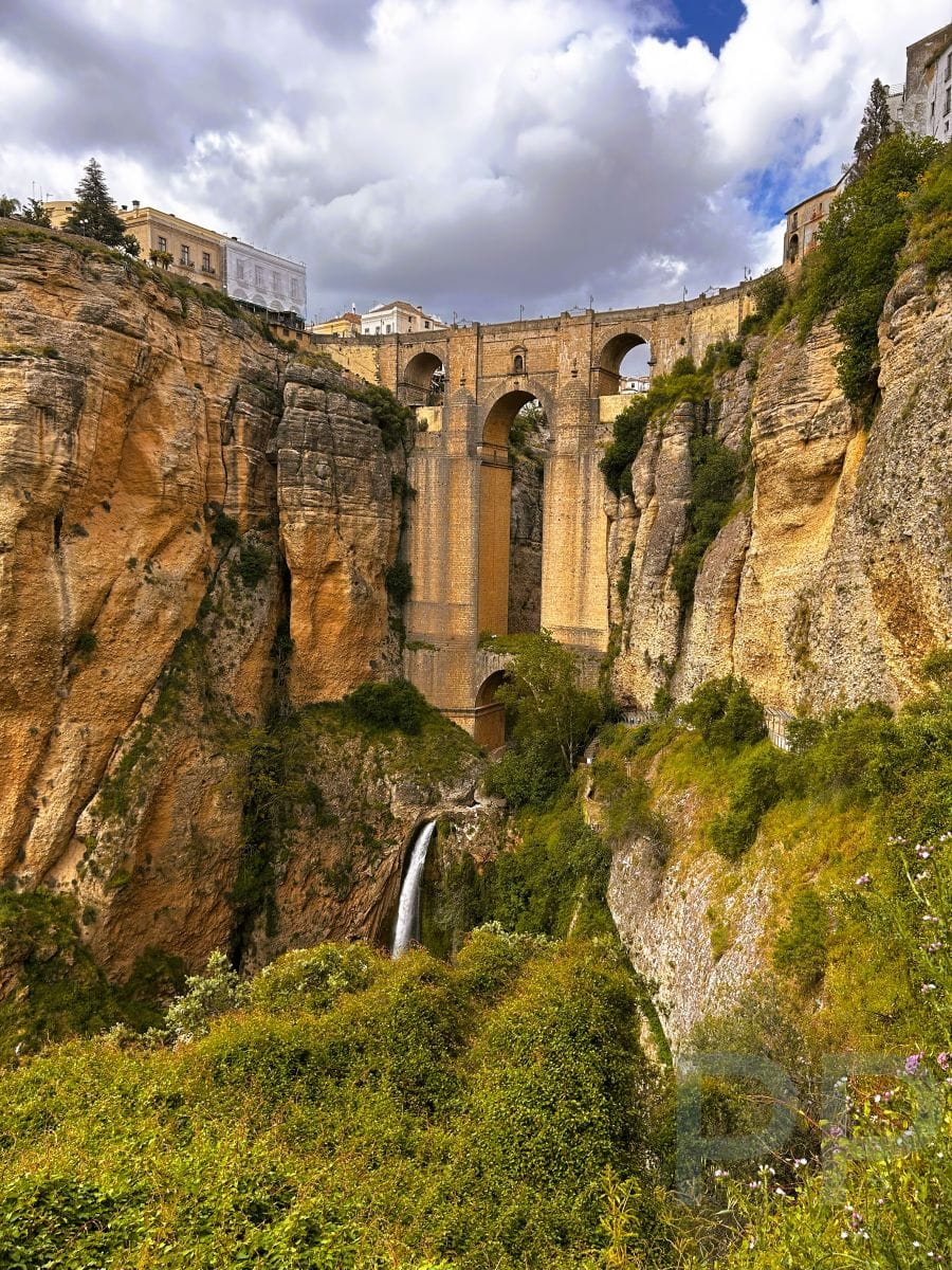 Wide view of Puente Nuevo bridge crossing the El Tajo Gorge in Ronda, Spain, with a waterfall flowing at the bottom of the canyon.