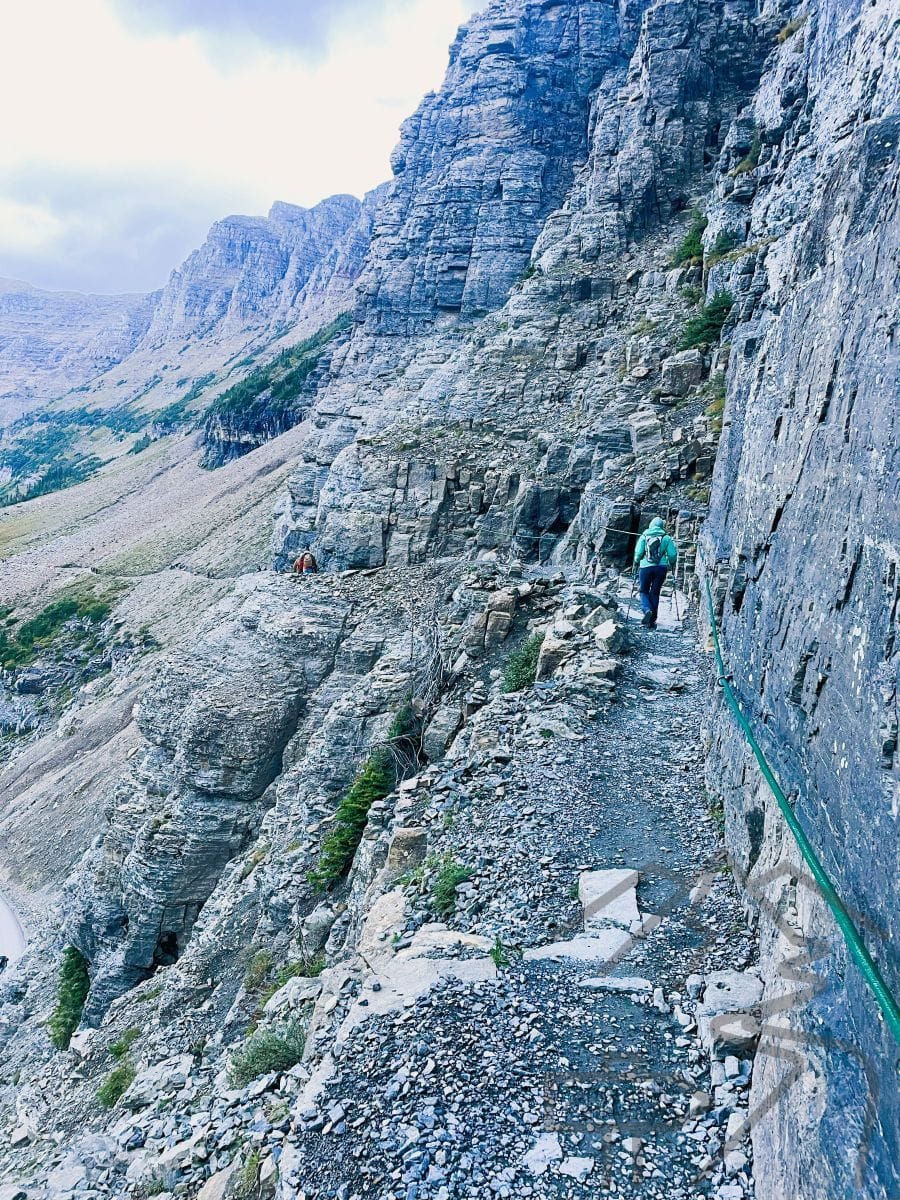 Hiker on the Highline Trail ledge section above the Going-to-the-Sun Road with green safety ropes.